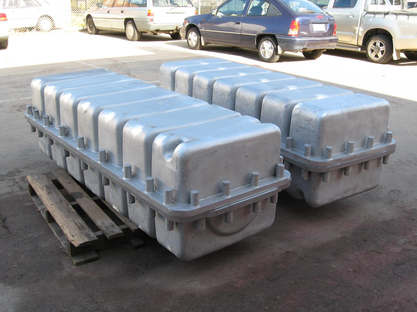 Two large, silver, fluted metal shipping containers with bolt flanges on wooden pallets outdoors.