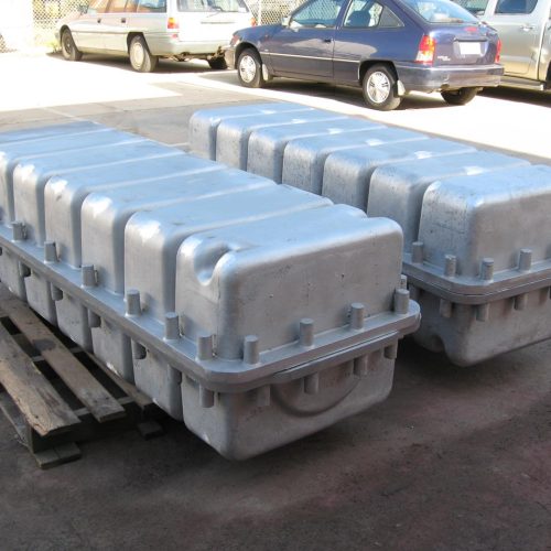Two large, silver, fluted metal shipping containers with bolt flanges on wooden pallets outdoors.
